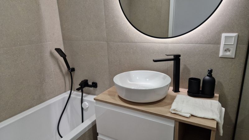 Fürdőszoba egy háromszobás lakásban kör alakú tükörrel és modern csaptelepekkel.