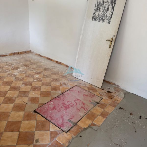 Szoba egy faházban cseréppadlóval és zsanér nélküli ajtókkal.