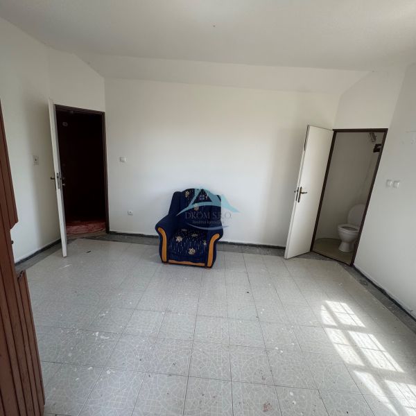 Szoba székkel, fehér falakkal, csempével és WC-be vezető ajtóval a házikóban.
