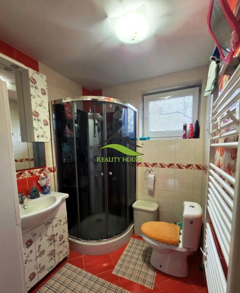 Fürdőszoba sarokzuhanyzóval, WC-vel és virágos dekorációval egy családi házban.