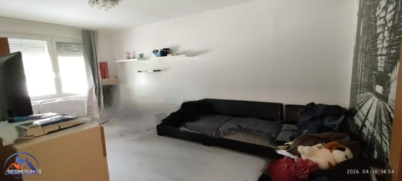 Nappali egy kétszobás lakásban fehér falakkal és fekete kanapéval.