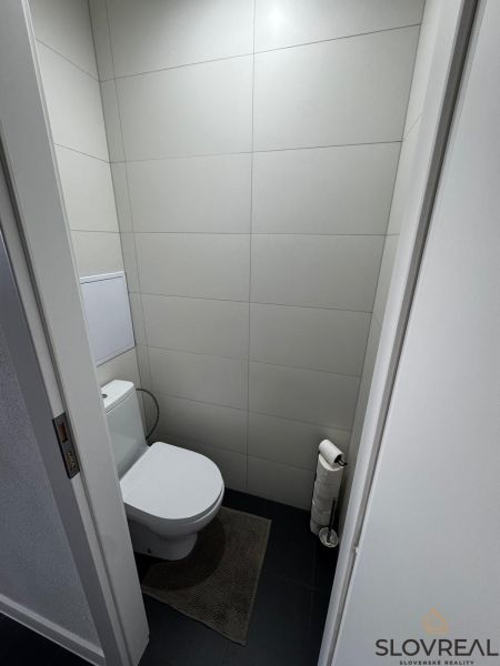 WC a háromszobás lakásban minimalista szürke csempékkel és sötét padlóval.