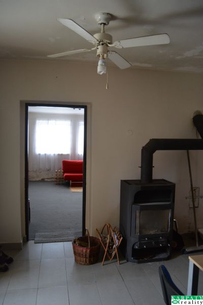 A családi házban van egy mennyezeti ventilátor, egy kályha és egy piros kanapé a háttérben.