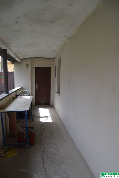 Folyosó fehér falakkal, repedések a padlón, asztal, ajtó egy családi házban.