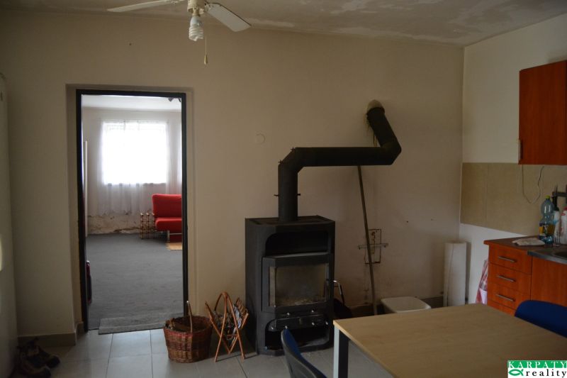 Családi ház belső tere kandallóval, ventilátorral és háttérben piros kanapéval.