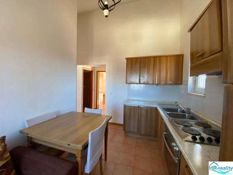 Nyaraló apartman konyhája fa szekrényekkel és étkezőasztallal.