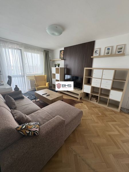 Nappali egy kétszobás lakásban fa mintázatú padlóval, kanapéval és TV szekrénnyel.
