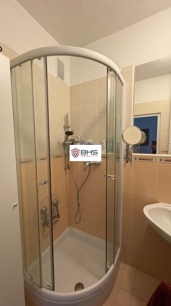 Fürdőszoba zuhanyzóval egy kétszobás lakásban, krémszínű csempékkel.