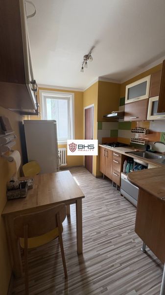 Konyha sárga falakkal, fa bútorokkal és fa mintázatú padlóval egy kétszobás lakásban.