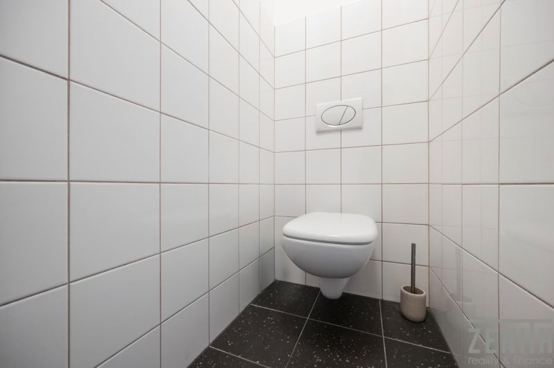 Fehér csempés és fekete padlós WC egy kétszobás lakásban.