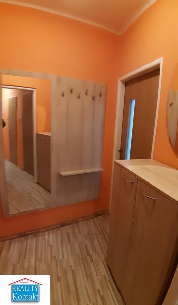 Narancssárga előszoba tükörrel, fogasokkal és fa dekoros padlóval egy kétszobás lakásban.