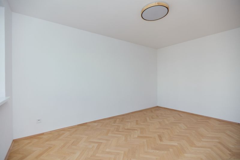 Egy üres szoba fehér falakkal és fa dekorációjú padlóval egy háromszobás lakásban.