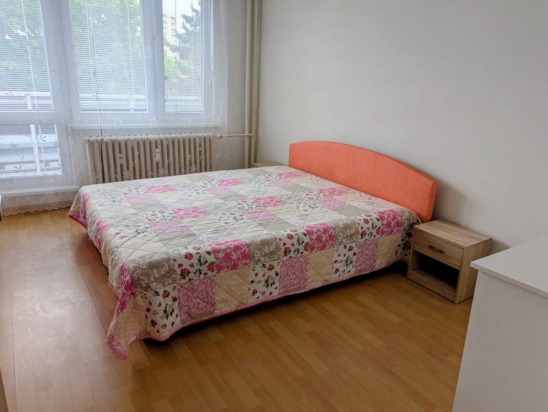 Hálószoba ággyal és patchwork ágytakaróval egy kétszobás lakásban, fa dekor padlóval.