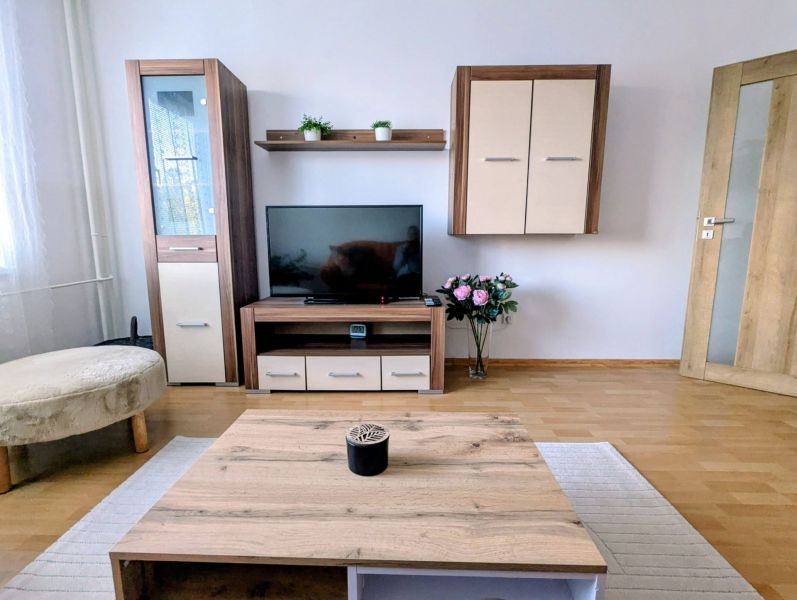 Kétszobás lakás nappalija fa mintázatú padlóval és TV bútorral.