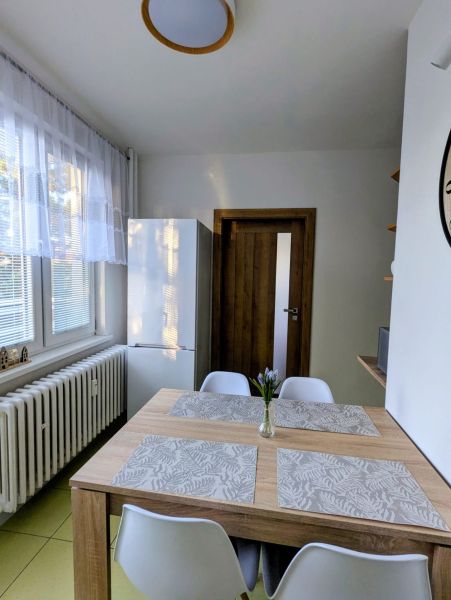 Étkező sarok egy kétszobás lakásban, fa asztallal és fehér székekkel.