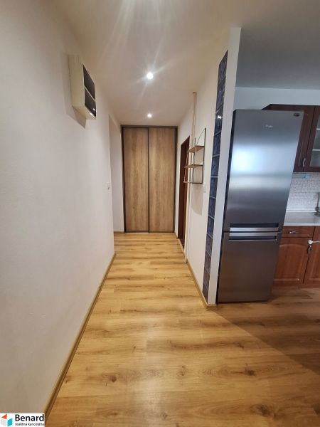 Előszoba beépített szekrénnyel és konyhával egy 2 szobás lakásban, fa padló, világos falak.