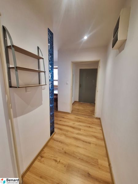 Folyosó egy kétszobás lakásban fa padlóval és polccal a falon.