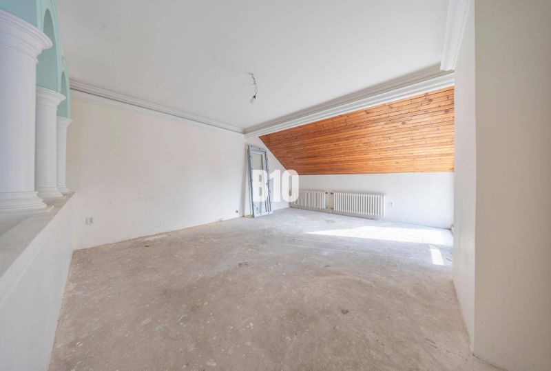 Tetőtéri családi ház fűtőtesttel és fa mennyezettel rendelkező, be nem rendezett szobája.