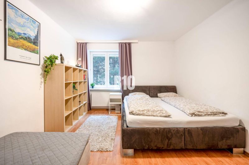 Hálószoba egy kétszobás lakásban ággyal, polccal, ablakkal és fa dekorációjú padlóval.