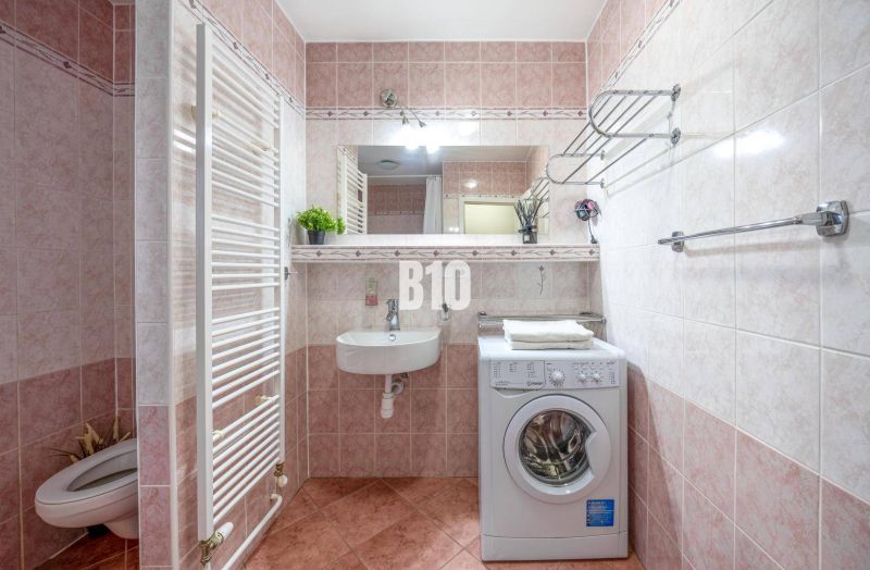 Fürdőszoba mosógéppel, mosdóval és WC-vel a kétszobás lakásban. Friss növények varázst kölcsönöznek.