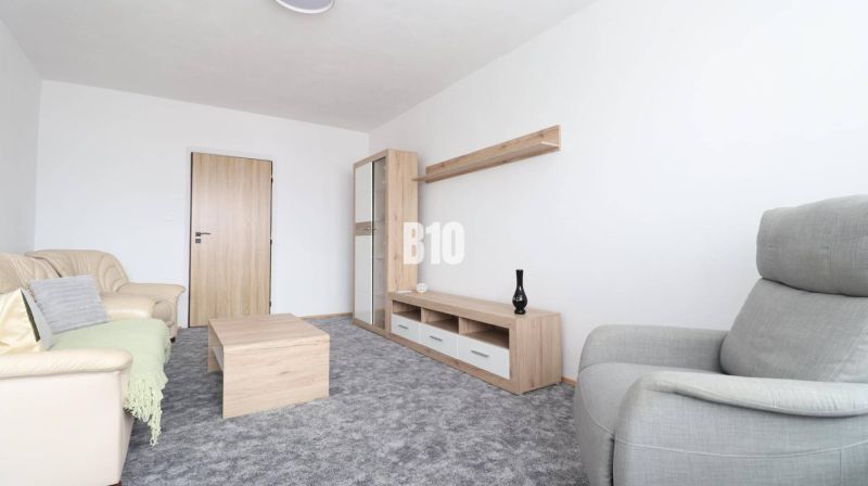 Nappali bézs kanapéval, szürke fotellel és fa dekorációjú bútorokkal egy háromszobás lakásban.