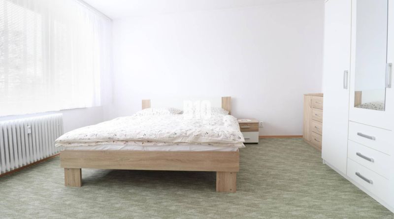Hálószoba egy háromszobás lakásban, franciaággyal, fehér bútorokkal és szőnyeggel.