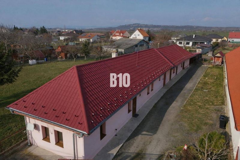 Egy családi ház Léva városában hosszú piros tetővel, kertek által körülvéve.