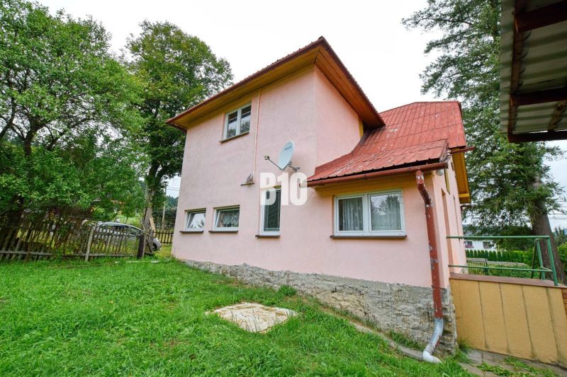 Családi ház Makovban rózsaszín homlokzattal, kerttel és műholdas antennával a falon.