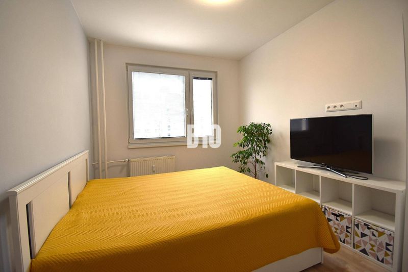 Hálószoba egy háromszobás lakásban, ággyal, televízióval és fa dekorációjú padlóval.