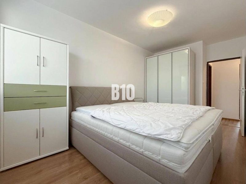 Világos szoba a nyaraló apartmanban ággyal, ruhásszekrényekkel és fa dekorációjú padlóval.