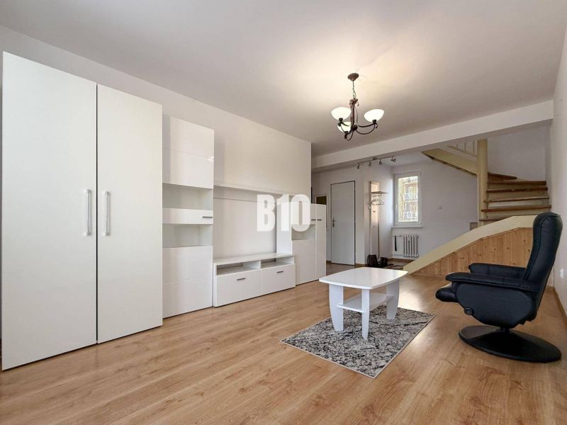Nappali a nyaraló apartmanban fehér bútorokkal és fa mintás padlóval.