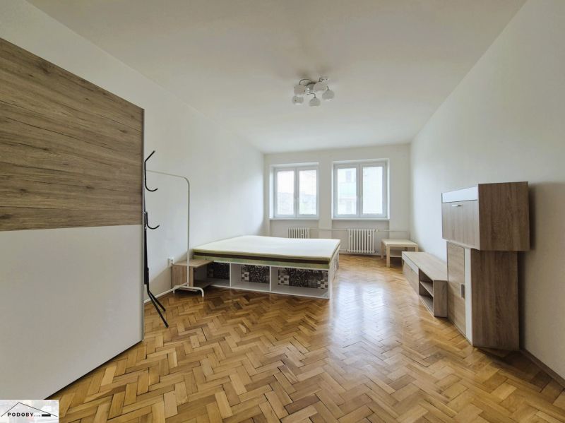 3 szobás lakás szobája ággyal és bútorral, fa mintázatú padlóval.