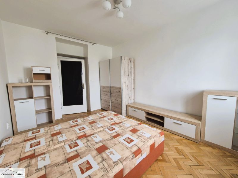 Hálószoba ággyal, tárolóbútorral és fa dekoros padlóval egy háromszobás lakásban.