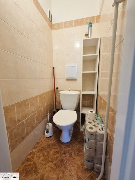 Fürdőszoba WC-vel, fehér csempékkel és polccal egy háromszobás lakásban.