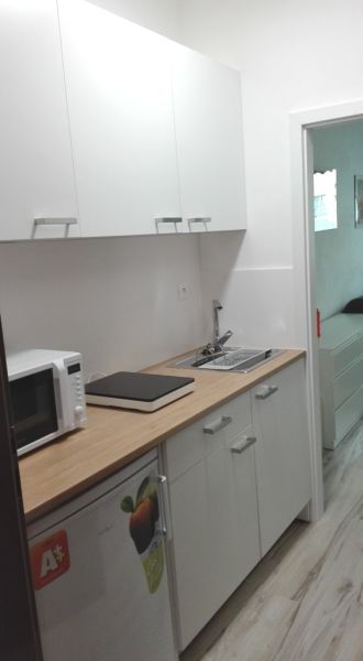 Konyhasarok a garzonlakásban szekrényekkel, mikrohullámú sütővel és fa mintázatú padlóval.