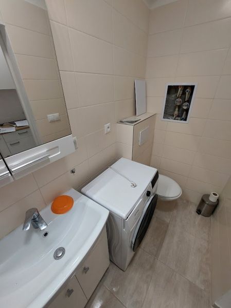 Fürdőszoba a garzonlakásban mosógéppel, mosdóval és WC-vel, világos falicsempékkel.