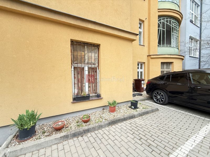 Parkolás az épület előtt a Leškova utcában, Pozsonyban, virágtartókkal és parkoló autóval.