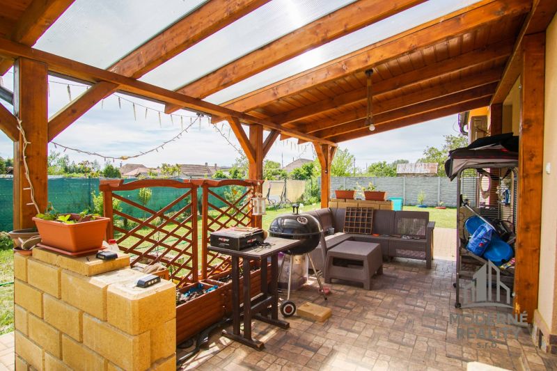 Andovciban, egy családi ház mellett terasz grillel és bútorokkal egy fa pergola alatt.
