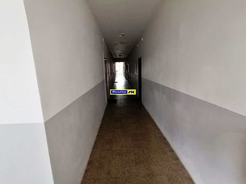 Hosszú folyosó fehér falakkal és csempézett padlóval egy egyszobás lakásban.