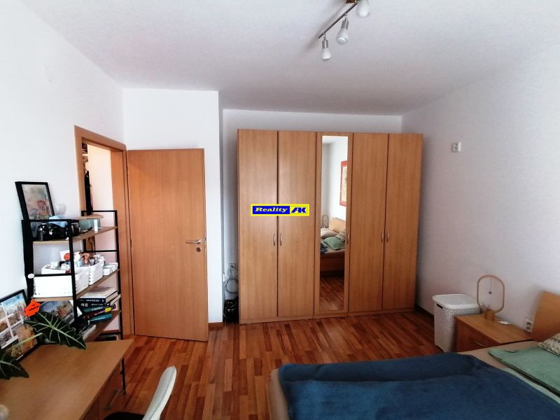 Hálószoba egy egyszobás lakásban, fa dekor padlóval, ruhásszekrénnyel és íróasztallal.