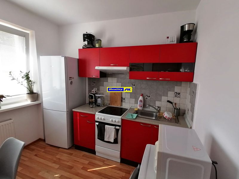 Konyha piros szekrényekkel és fa dekorációjú padlóval egy egyszobás lakásban.