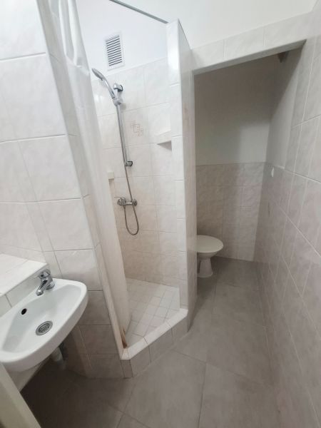 Fürdőszoba mosdóval, zuhanyzóval és WC-vel világos csempeszínekben, 1 szobás lakás.