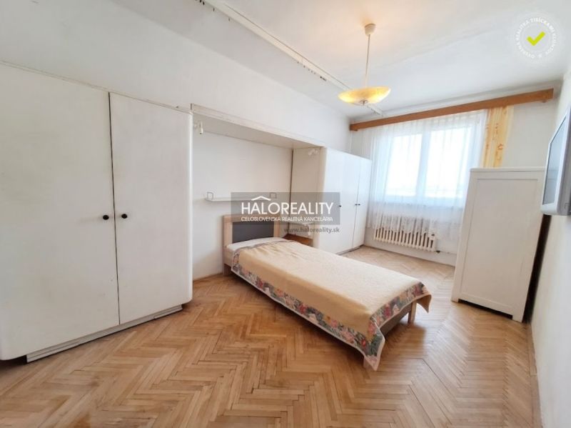 Hálószoba egy háromszobás lakásban, fa dekoros padlóval és egyszerű berendezéssel.