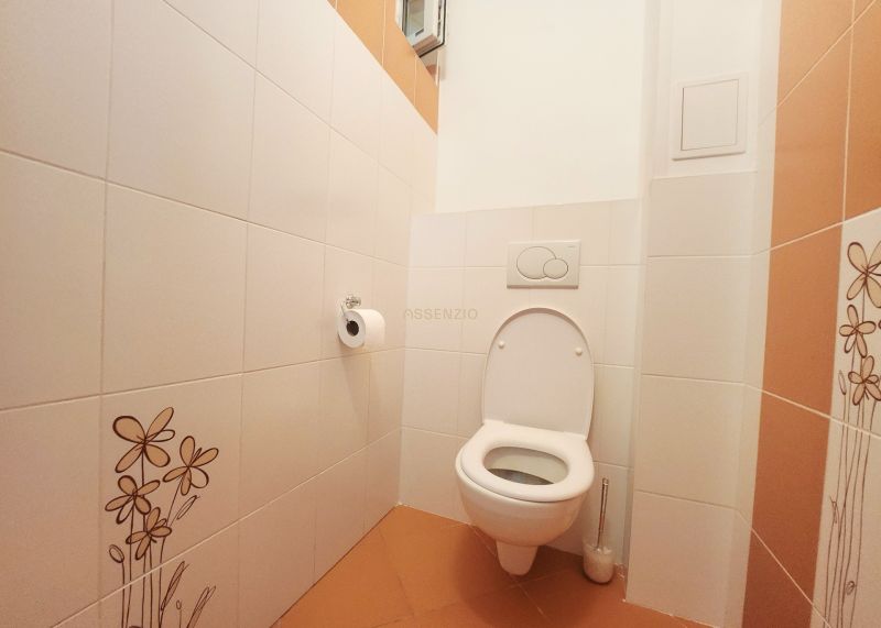 Fehér csempékkel és narancssárga padlólapokkal ellátott WC egy háromszobás lakásban.