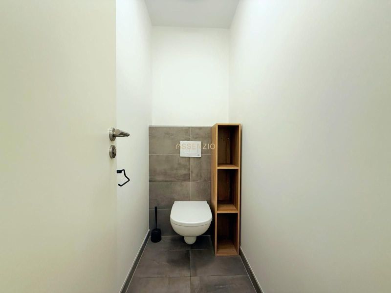 WC szürke csempével és fa polccal egy kétszobás lakásban.