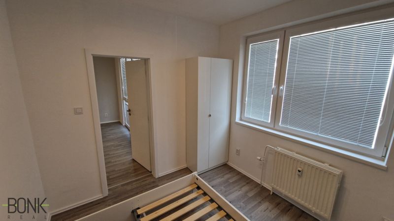 Hálószoba egy kétszobás lakásban fehér falakkal és fa mintázatú padlóval.