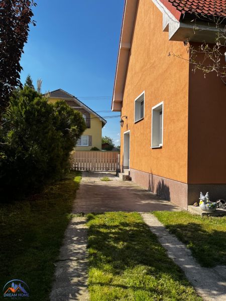 Családi ház Csallóközben narancssárga homlokzattal, gyepesített udvarral és szilárd burkolatú bejárati úttal.