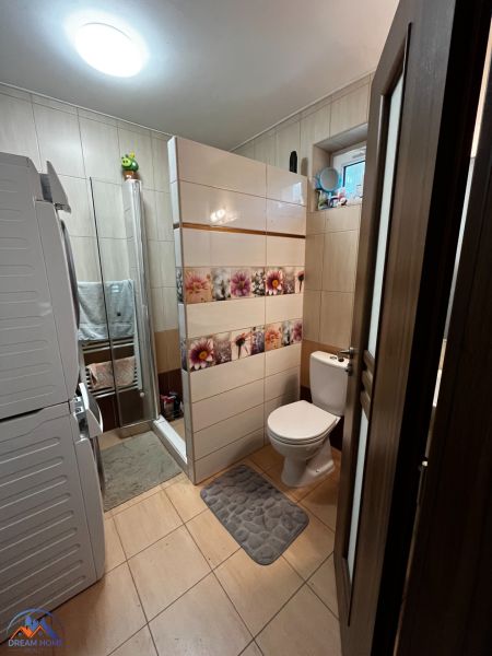 Családi ház fürdőszobája mosógéppel, zuhanyzóval és WC-vel.