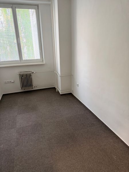 Irodai szoba szőnyeggel, radiátorral és redőnyös ablakkal.