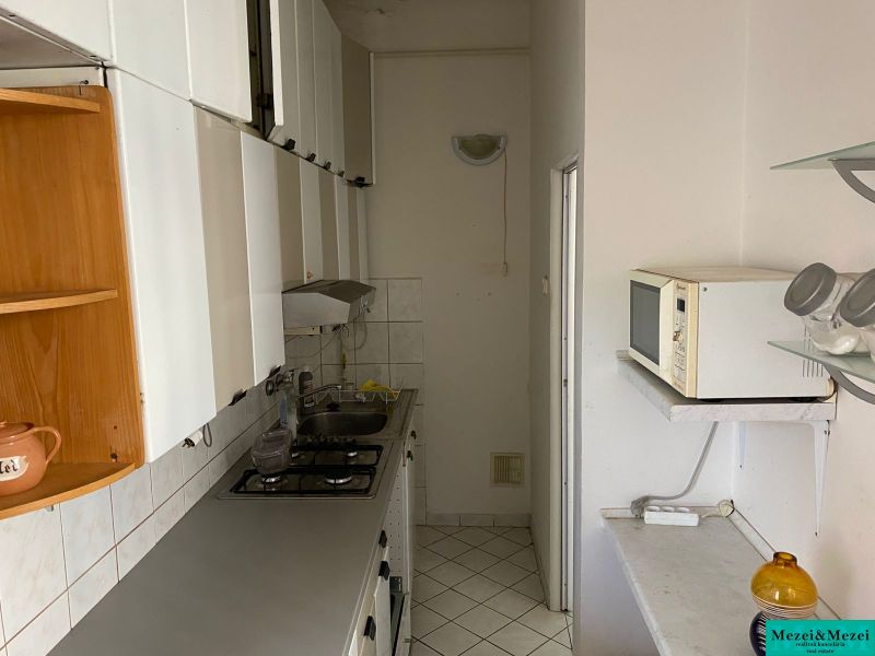 Keskeny konyha egy kétszobás lakásban fehér bútorokkal és csempékkel.